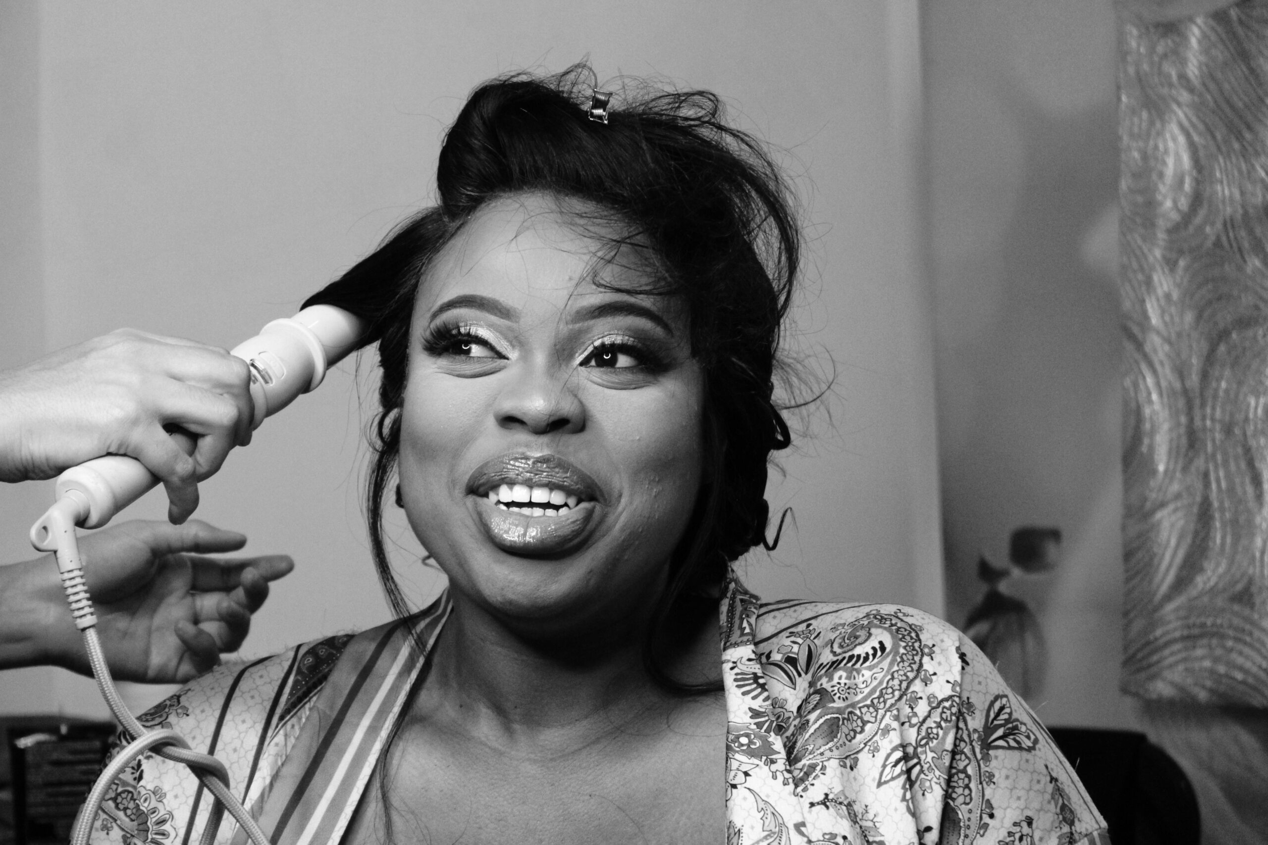 Black and white portrait of a woman having her hair styled, exuding joy and beauty.